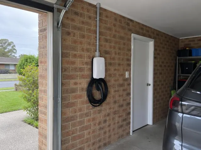 Wall-mounted EV charger and coiled cable on a brick garage wall beside a door in Beresfield